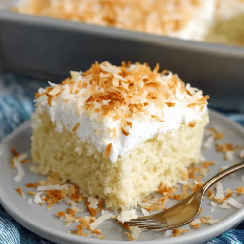 Delicious Coconut Poke Cake topped with Cool Whip and shredded coconut.